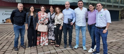 Ocho personas posan sonrientes frente a un edificio acristalado, sobre una plaza adoquinada; visten ropa formal e informal.